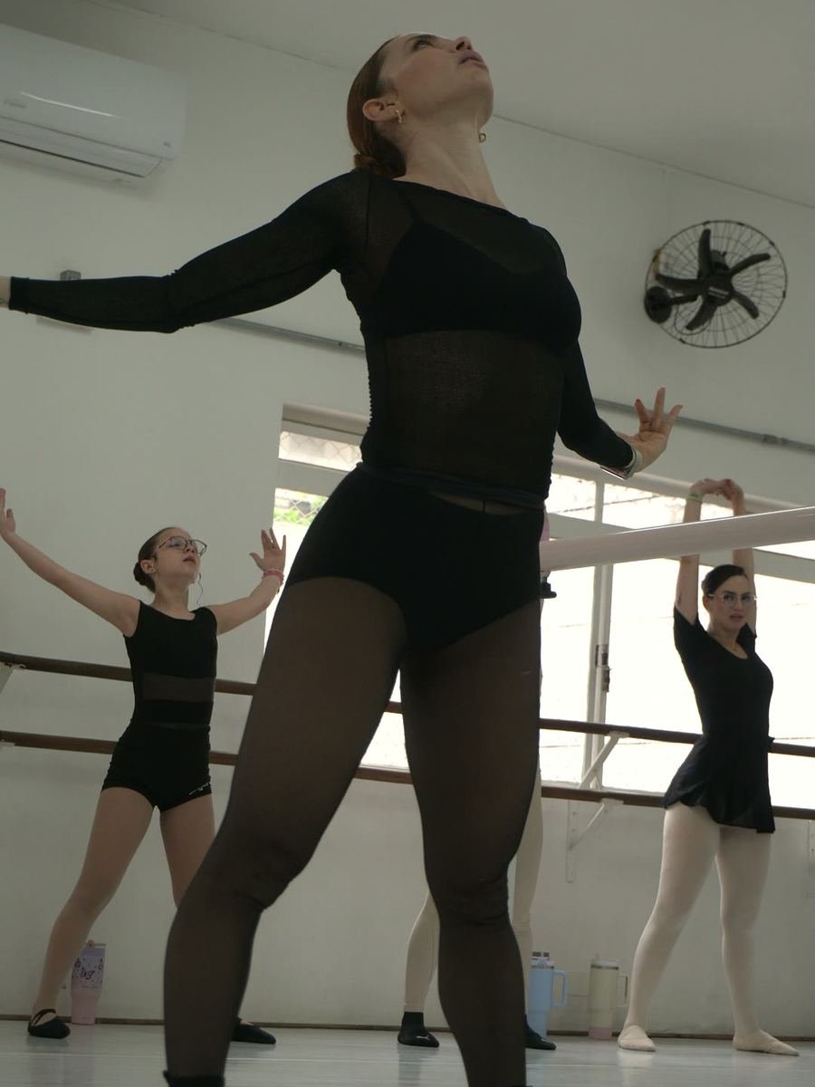 Renata dançando de braços abertos e cabeça para trás, com a turma ao fundo